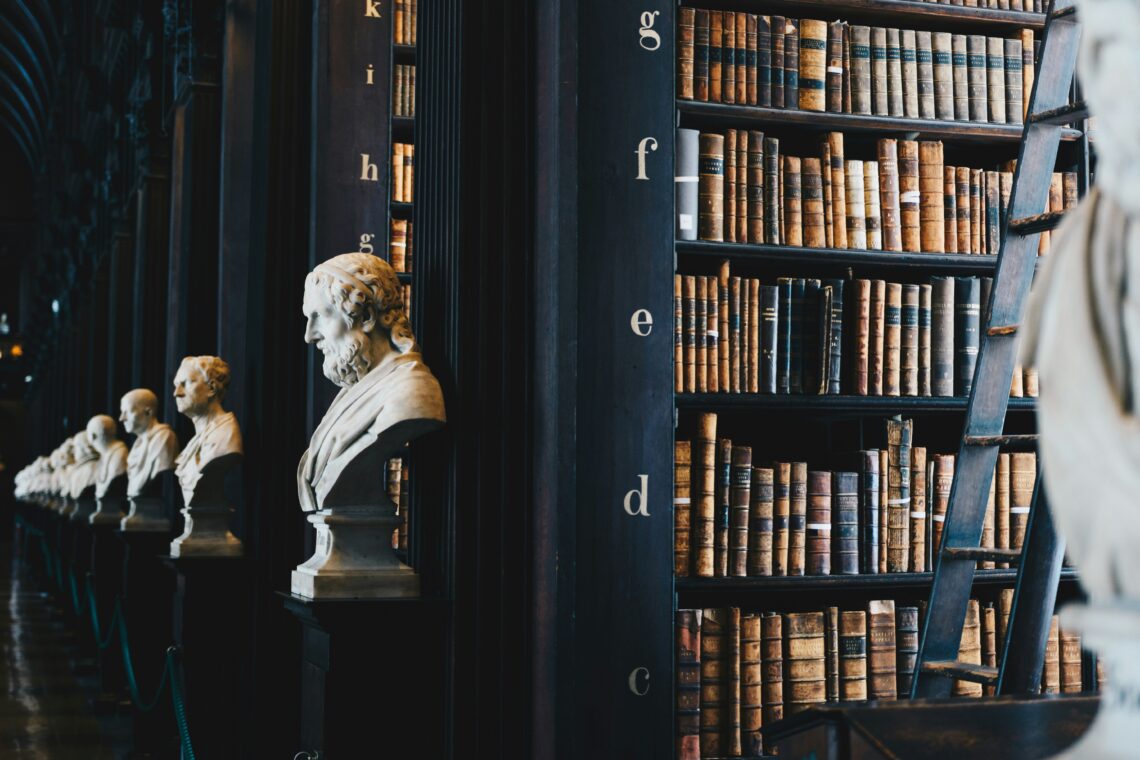 Dark library with statues on the ends of bookshelf rows