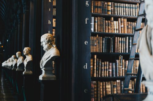 Dark library with statues on the ends of bookshelf rows